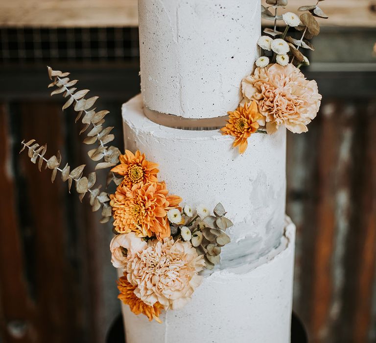 Speckled taupe buttercream wedding cake with bright orange flowers and dried eucalyptus decor