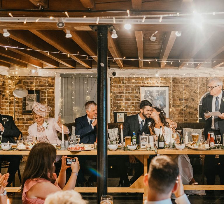 Wedding guests during reception in rustic venue surrounded by fairy lights 