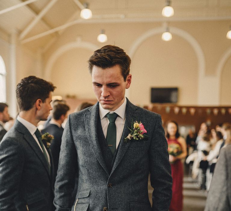 Pensive groom in a dark grey tweed wedding suit standing at the altar waiting for his bride to arrive 