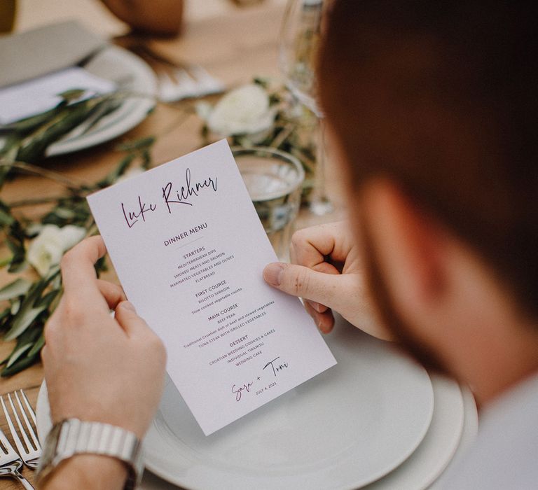 Wedding guest reads wedding menu on traditional white stationery 