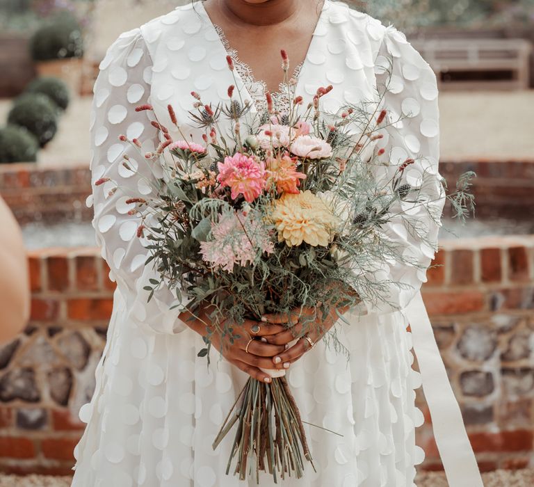 Bride in long mesh sleeved spotted Vagabond wedding dress and bridal hair bow holding mixed fresh and dried bouquet before Wasing Park wedding ceremony