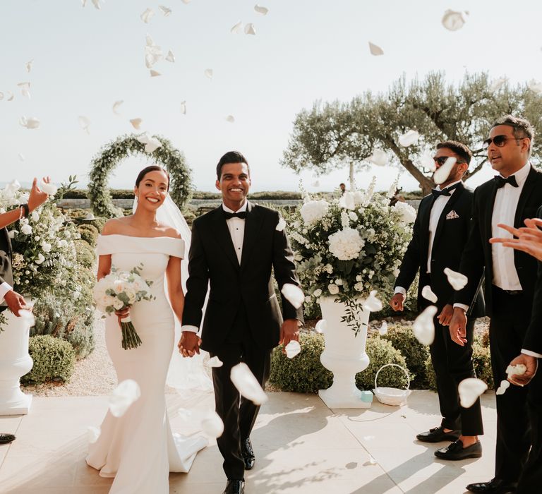 Bride & groom walk down the aisle hand in hand as wedding guests throw white rose petals around them | Hannah MacGregor Photo & Film