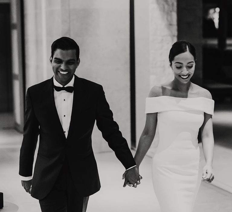 Bride & groom walk hand in hand as bride wears off-the-shoulder wedding gown in black & white photo | Hannah MacGregor Photo & Film