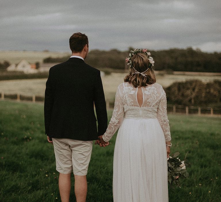 Bride and groom wedding portrait in a field with the groom in shorts and the bride a floaty dress and flower crown 