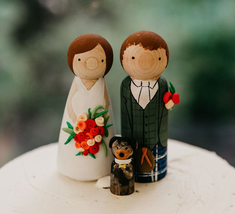 Wooden peg wedding cake toppers with bride holding flower, groom in a kilt and a pet dog 