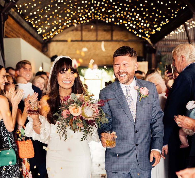 Bride & groom walk down the aisle as wedding guests throw confetti around them 