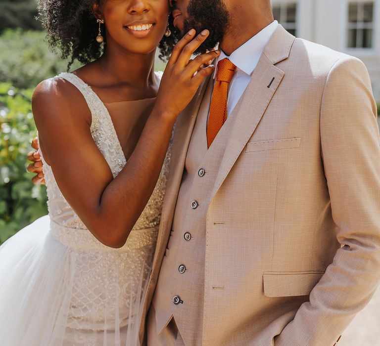 Black groom in a beige three-piece suit kissing his bride's cheek with naturally curly hair in a princess wedding dress