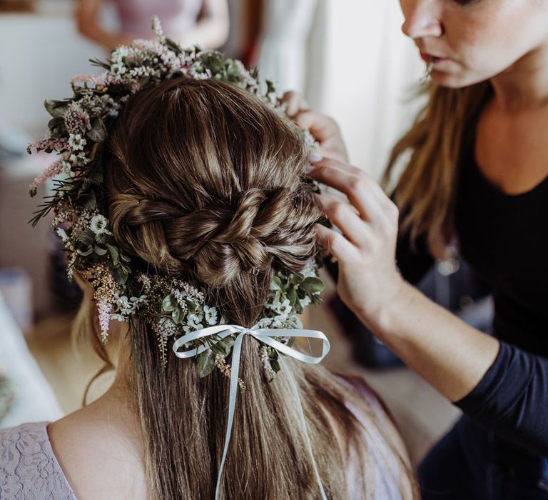 Bridesmaid with braided hair has dried flower crown fixed to her head by hair stylist before wedding ceremony