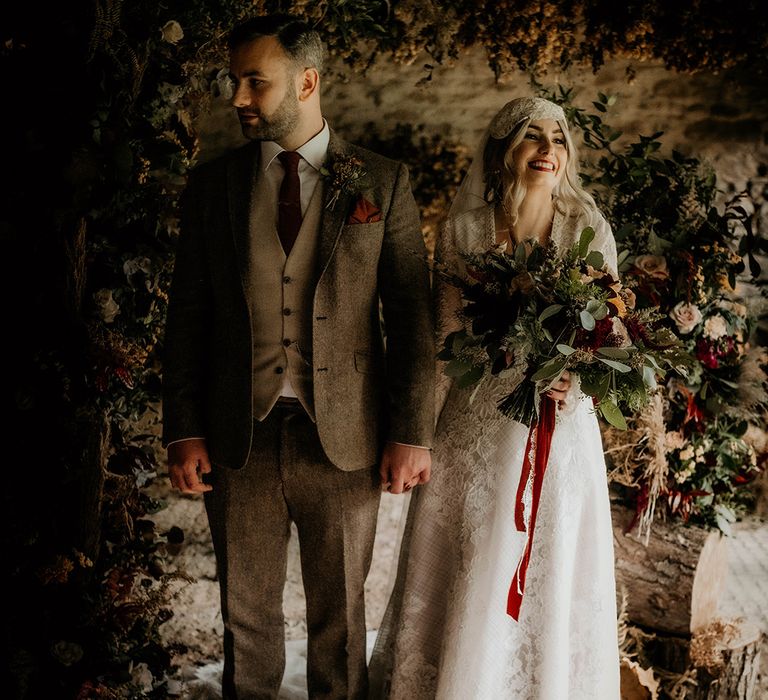 Bride in a lace wedding dress and Juliet cap veil holding hands with her groom in a wool suit at the altar of their Lyde Court wedding