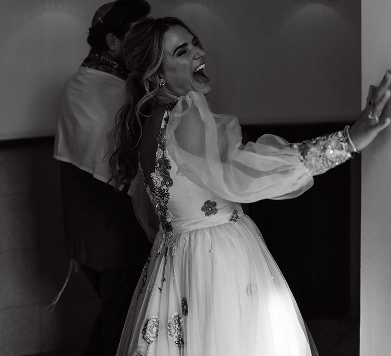 Bride in mesh sleeve embroidered wedding dress laughs as her and groom leave wedding ceremony