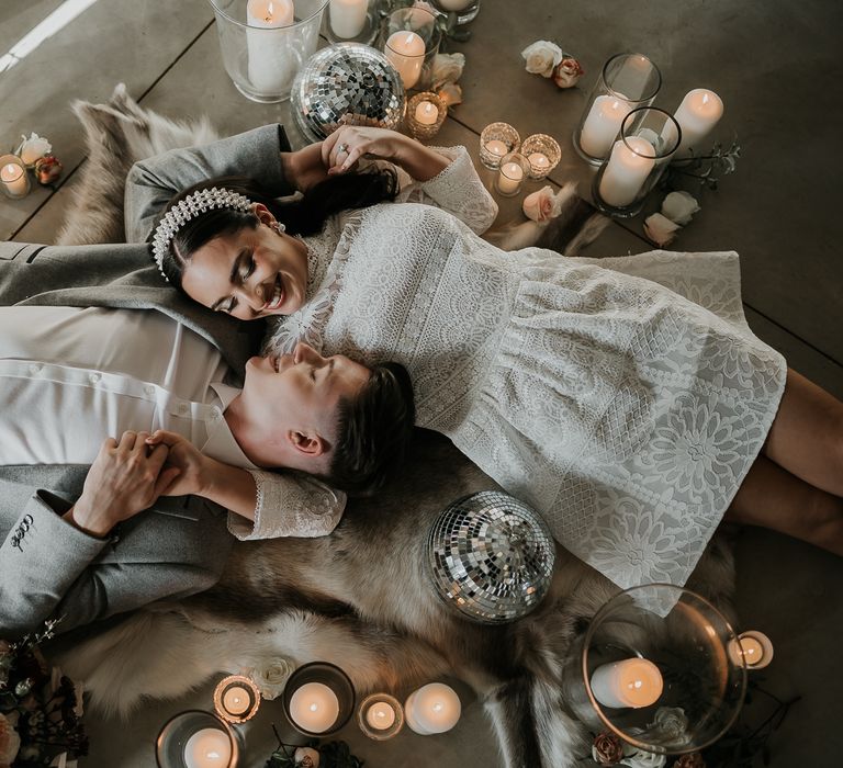 Bride & groom lay down on the floor next to pillar candles, fur rug and disco ball decoration