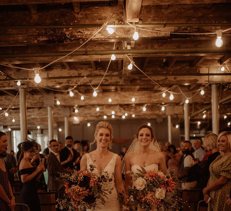 Brides walk with one another holding large floral bouquet with oranges and whites