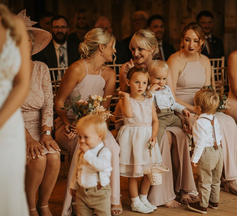 Bridesmaids in light pink halter neck bridesmaid dresses stand with flower girl and boys in white shirts and braces