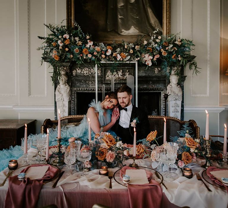 Luxe black tie wedding at Newburgh Priory with bride in a coloured ruffle wedding dress and groom in a tuxedo sitting at their wedding reception table full of candles and flowers 