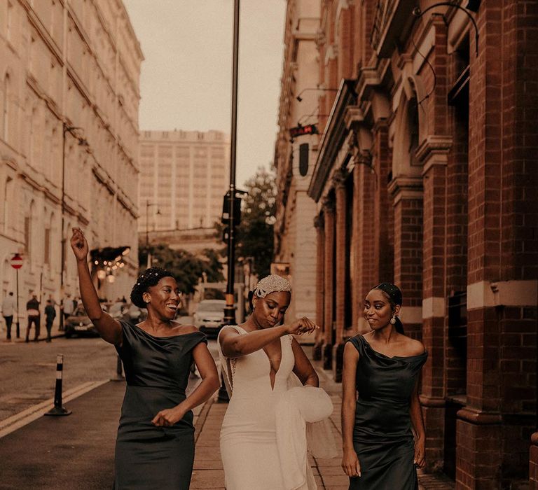 Bride in a fitted Pronovias wedding dress dancing through the streets of Birmingham with her bridal party in navy satin bridesmaid dresses 