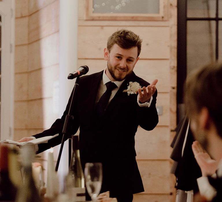 Groomsman gives a speech at the wedding in black tie and dried flower boutonnière