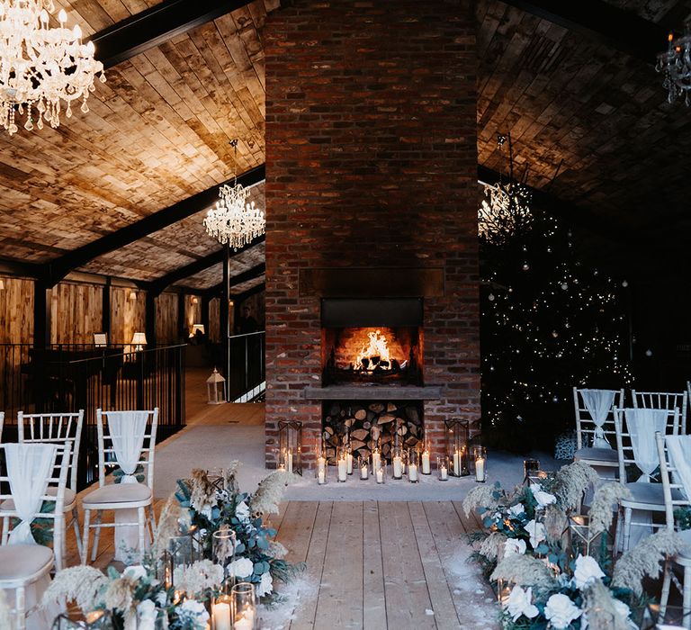 Cosy open fireplace with Christmas tree, chandeliers, dried flower decorations and candle lanterns fir wedding ceremony 