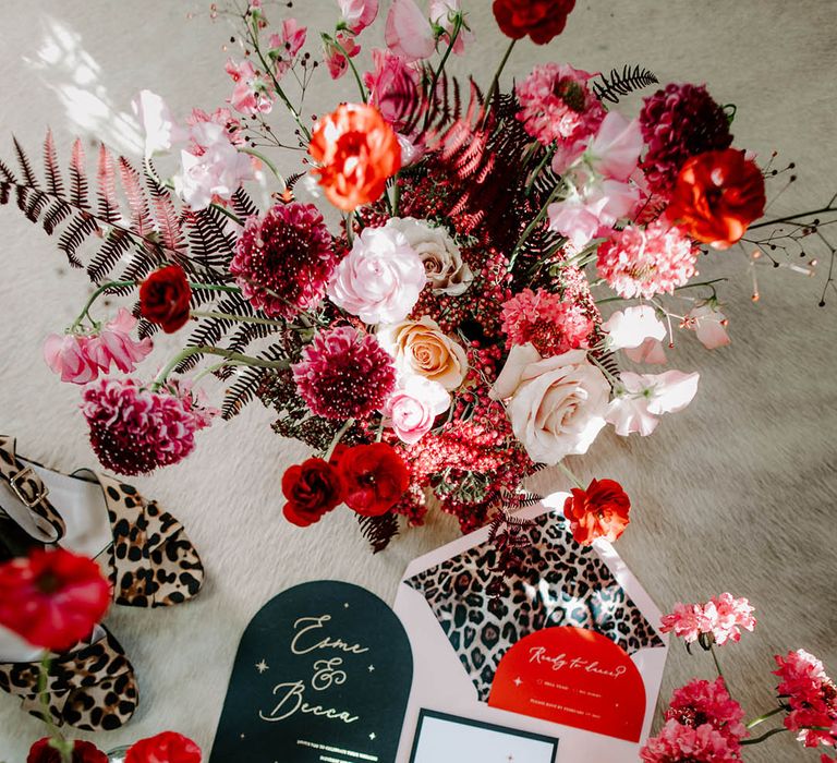 pink and red flowers and flatlay of wedding stationery suite with leopard print lined envelopes and goild foil lettering and tassel detail 