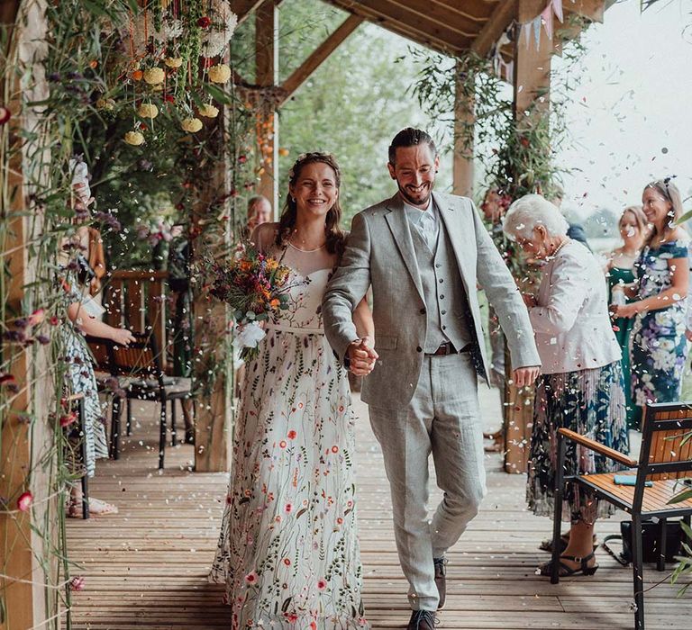 Bride and groom walk through confetti at their botanical outdoor wedding 