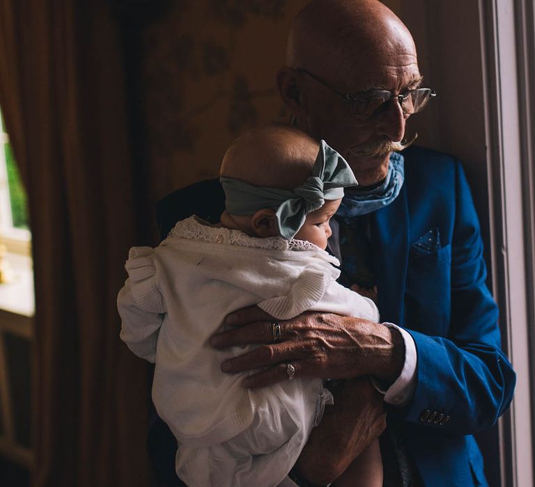 Wedding guest in blue suit holds baby with blue bow headband