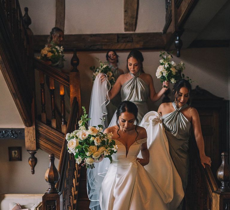 Bridesmaids in halter neck mint green bridesmaid dresses help the bride down the stairs by lifting the train of her gown