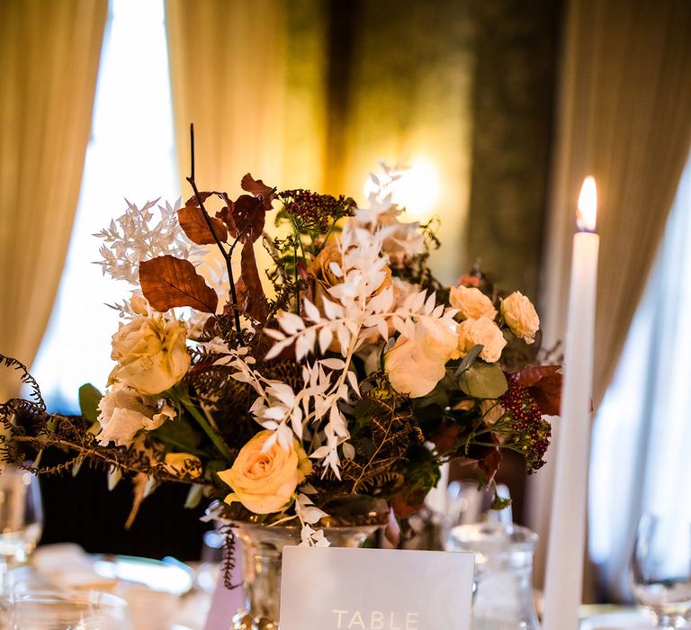 White frosted table number sign with white mugs and candles with gold candle holders and rose centrepieces