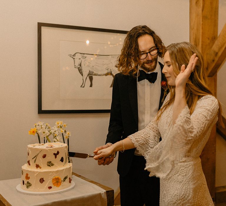 Bride and groom cut their two-tier cake in white frosting with flowers and mini daffodils