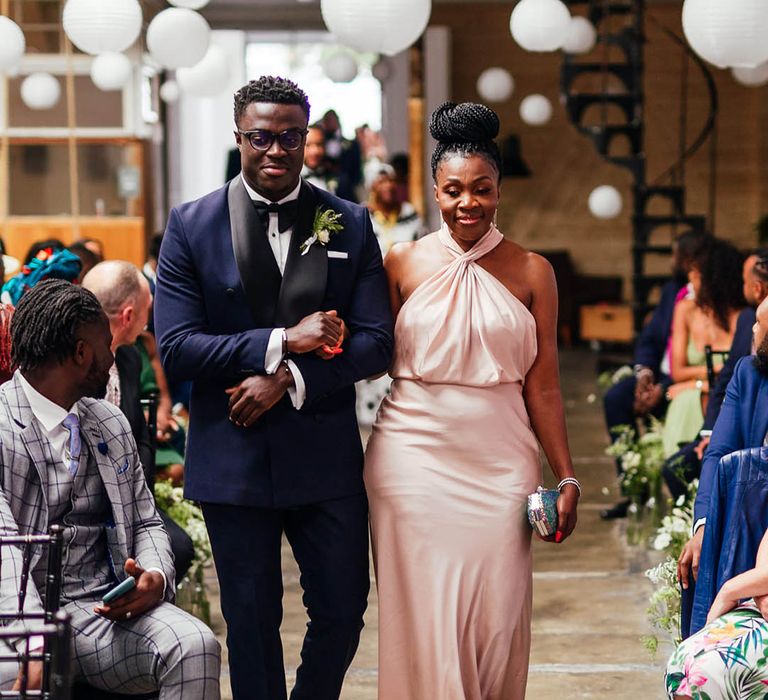 Bridesmaid in pale pink halter neck satin dress walked down the aisle with groomsmen in blue tuxedo 