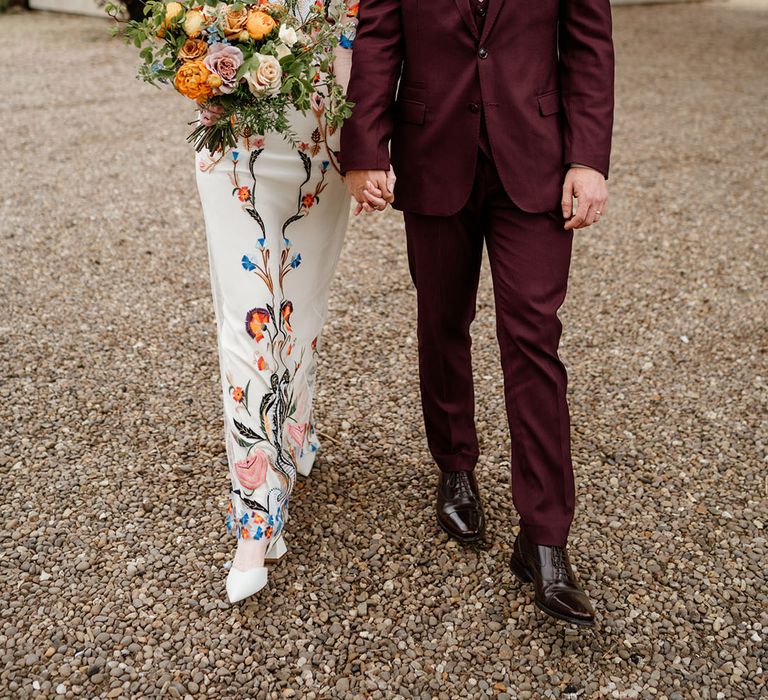 Groom in three piece burgundy suit with patterned tie with bride in white wedding dress with bright and colourful flowers 