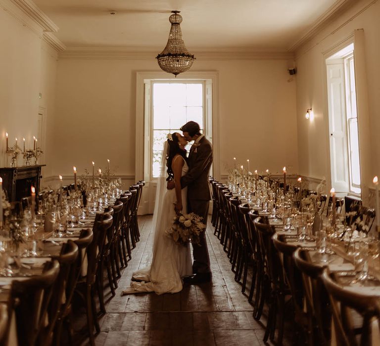 Bride and groom share a kiss in their wedding reception room with banquet tables and dried flower minimal decor 