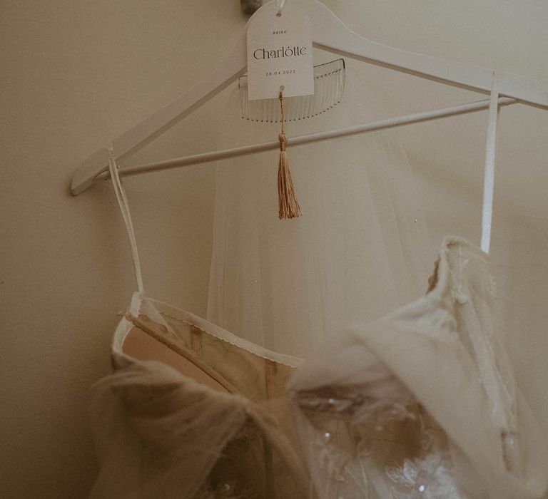 White coat hanger with name tag with the bride's feather tulle wedding dress and veil 