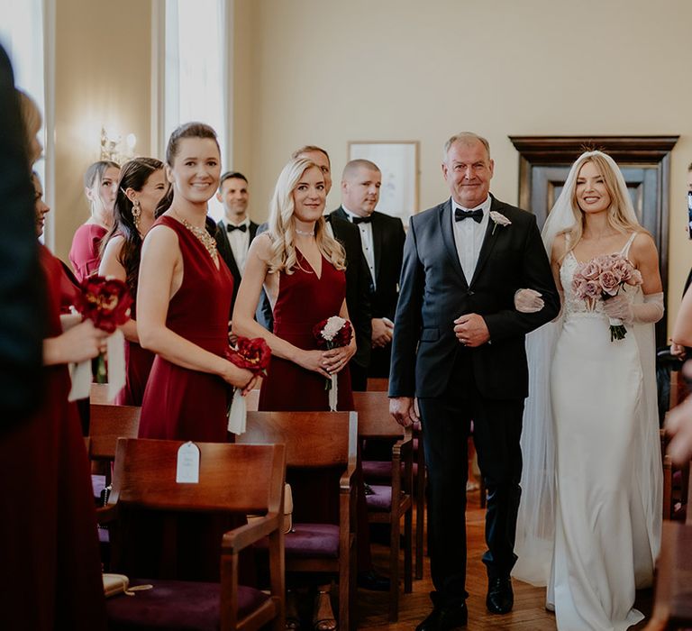 Father of the bride in black tie walks the bride in beaded deep v wedding dress down the aisle 