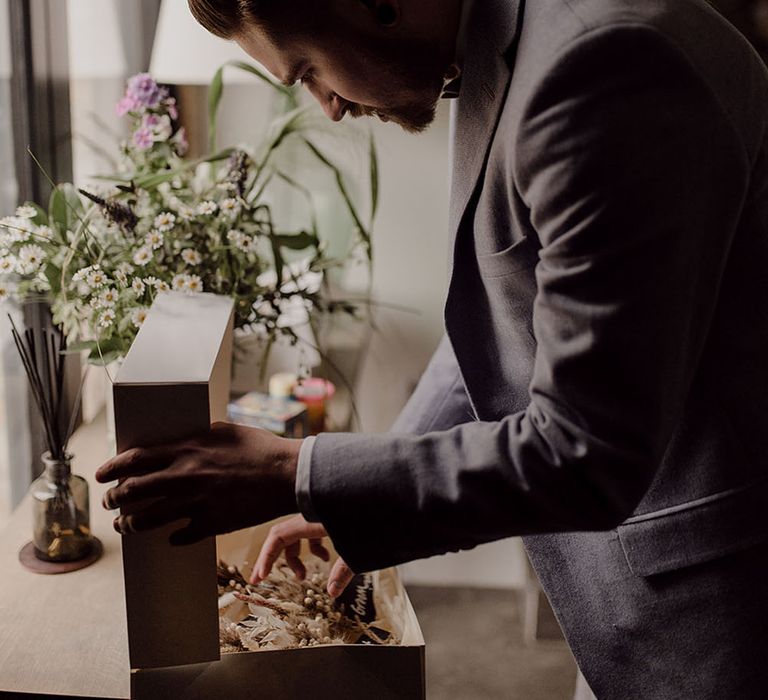 Groom opens wooden box revealing dried floral buttonholes 