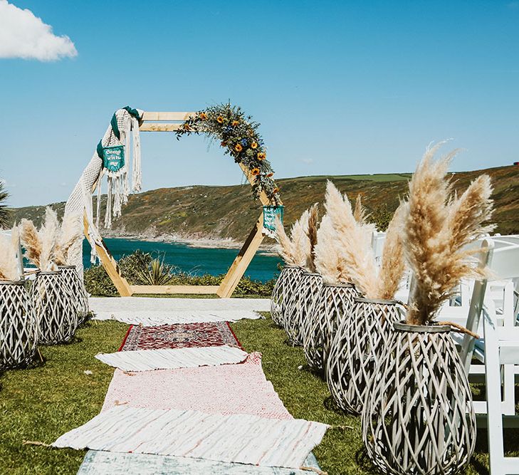 Wicker vases holds pampas grass bouquets lining aisle with Moroccan styled rugs and DIY wooden arch 