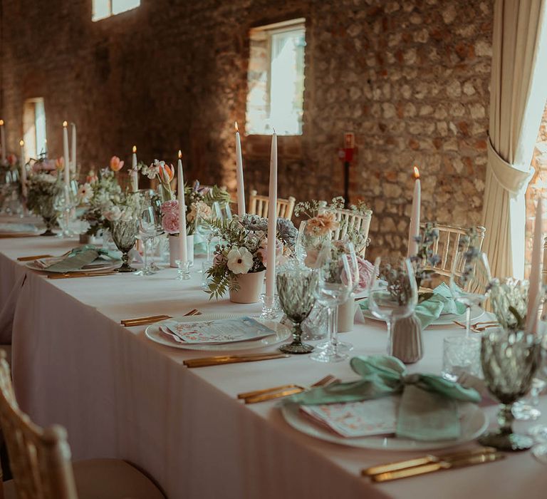 Pale pink taper candles and flowers with green napkins and ribbons with copper cutlery 