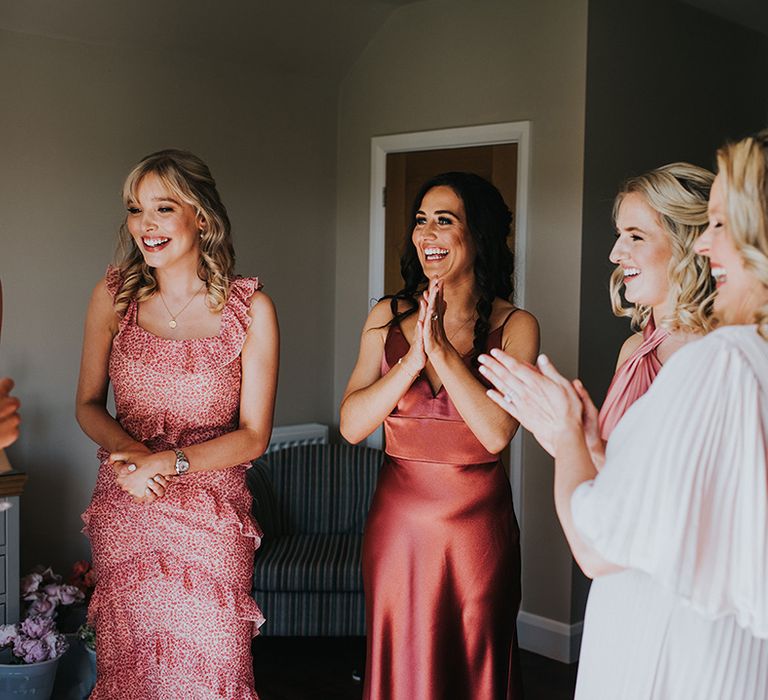 Bridesmaids smile and clap as they get their first look at the bride on her wedding day 