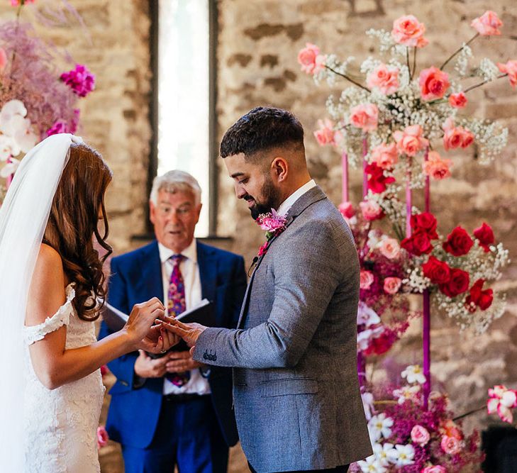 Bride & groom stand in front of bright pink floral wedding arch at the Priston Mill during wedding ceremony 