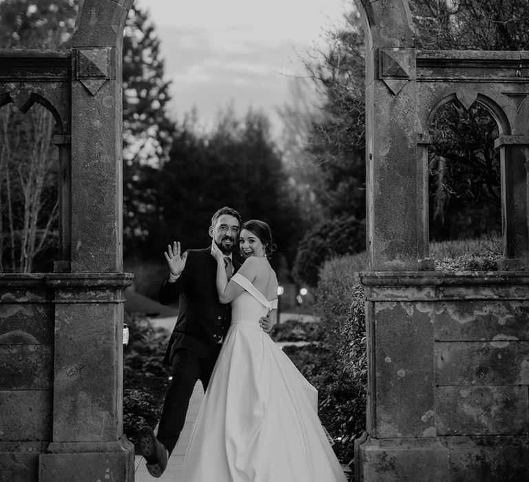 Bride and groom pose together under an arch 