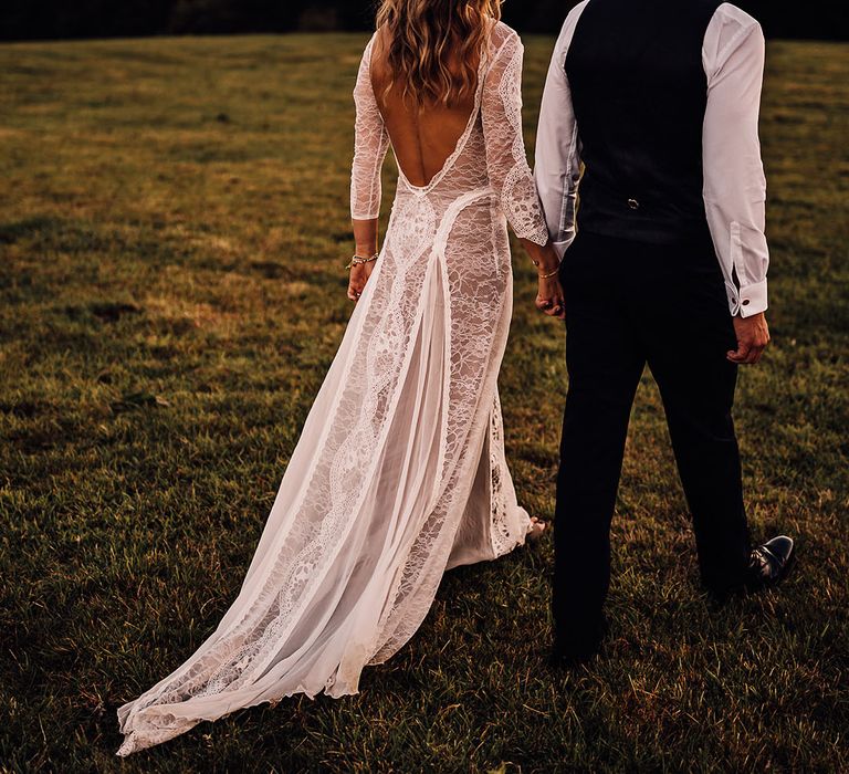 Bride in a low scoop back lace wedding dress walking with the groom in black tie 