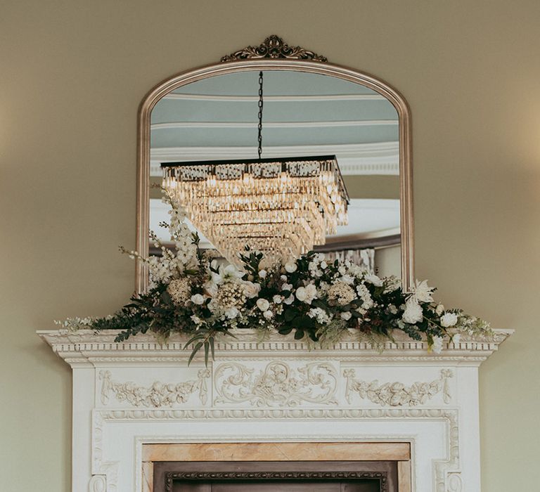 Large white and bronze fireplace decorated with faux wedding flowers and vases filled with water and floating tea lights