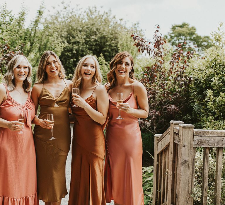 Bridesmaids in mismatched olive, rust and orange coloured dresses 