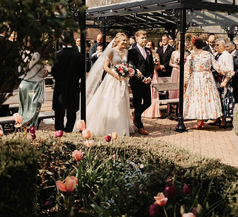 Bride in a lace wedding dress is escorted down the aisle for her outdoor wedding ceremony 