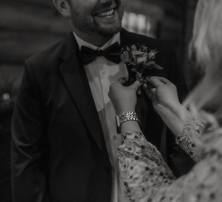 Groom in black tie gets his buttonhole put on for the wedding day 