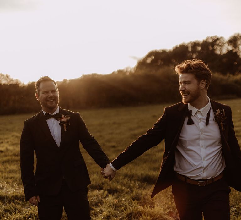 Grooms walk laughing holding hands during sunset captured by LGBTQ photographer