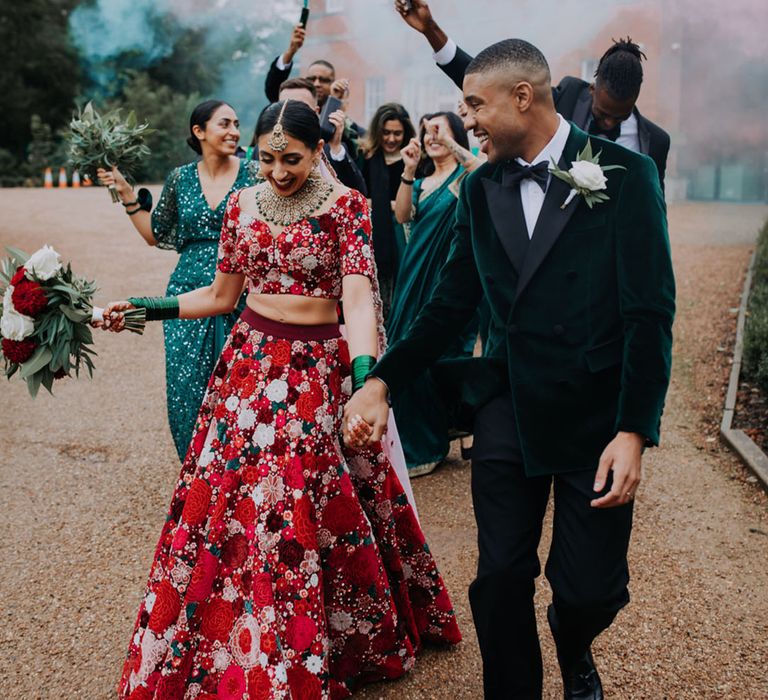 Bride wearing traditional Indian wedding outfit in a bold magenta walking with the groom as they have a smoke bomb entrance 