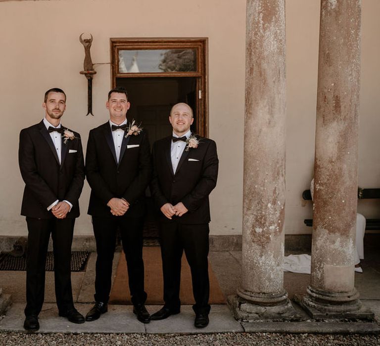 Groom and groomsmen all in matching classic black tie and soft pink buttonholes