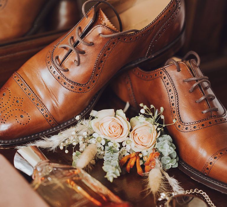 Brown brogue wedding shoes beside pastel peach rose buttonhole and silver pocket watch 