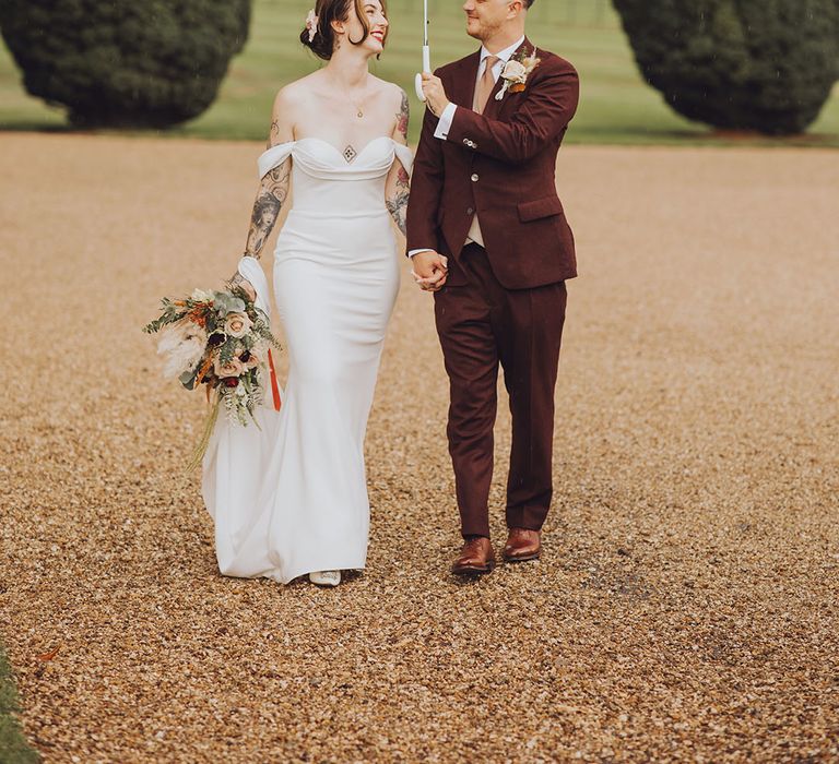 Groom holds clear umbrella above his bride wearing Vera Wang wedding dress and holding Autumnal bouquet 