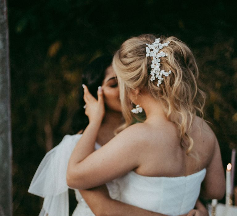 Bride in sleeveless tulle layered wedding dress and bride in short puff sleeve lace wedding dress kissing at the alter of Holesfoot