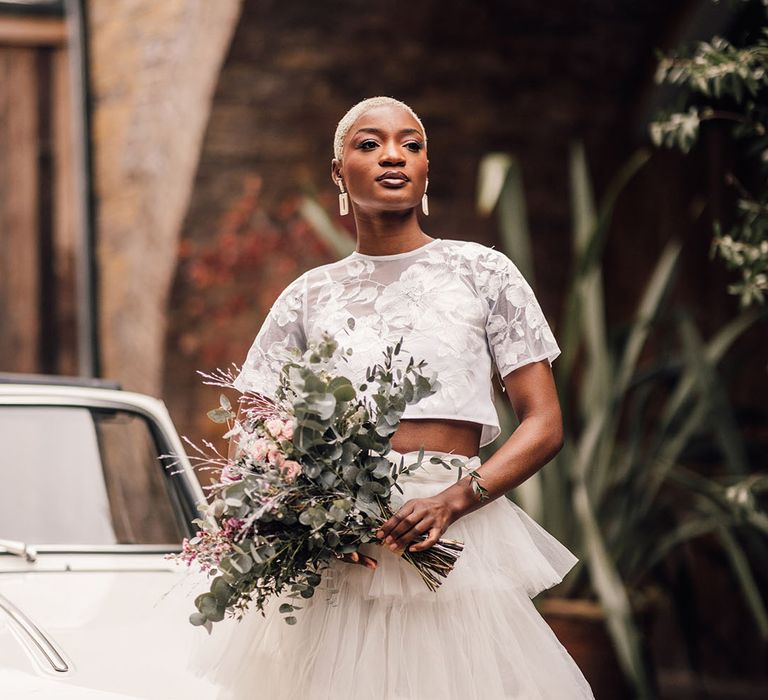 Bride wears a bridal two piece set whilst carrying bouquet featuring eucalyptus, pink roses and waxflower